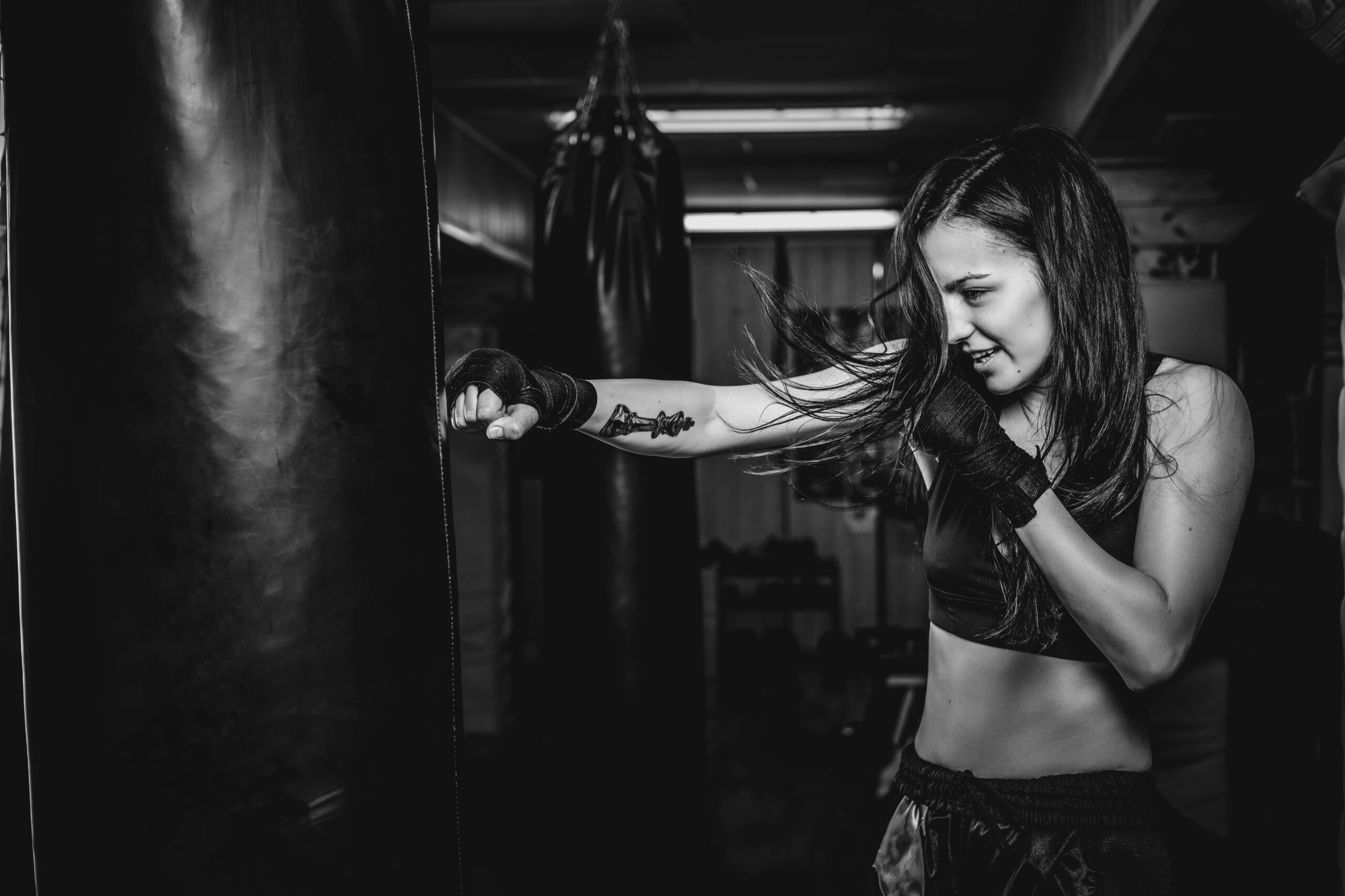 Happy smiling girl has a boxing training at gym with punching bag, black and white photo.